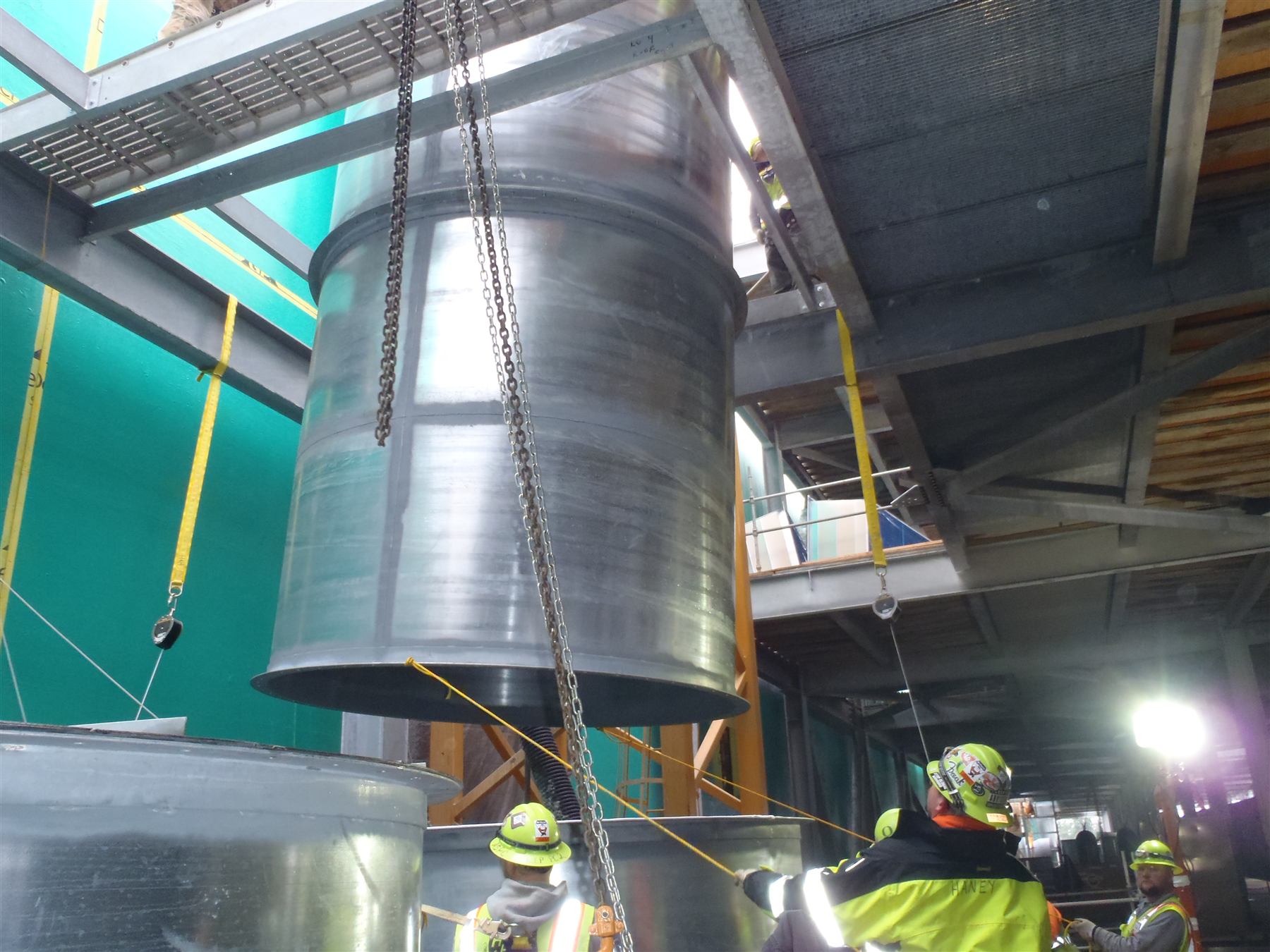 Harris & Hart crew in hard hats and hi-vis rigging a large duct section with chain hoists and tag lines