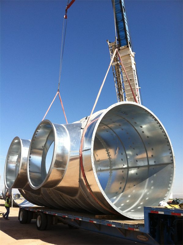 Crane lifting a large galvanized duct fitting off a flatbed trailer
