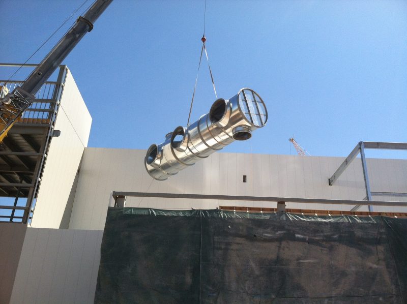 Crane lifting a round duct manifold with branch outlets up to a building roof