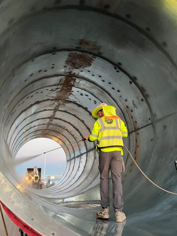 Worker in hi-vis gear pressure-washing the inside of a large round duct section
