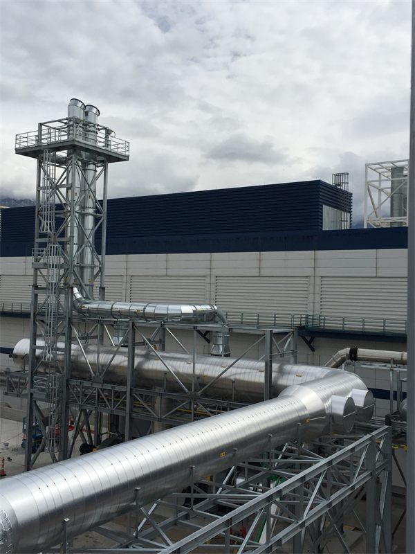 Twin exhaust stacks in a steel tower with large insulated duct headers on a pipe rack