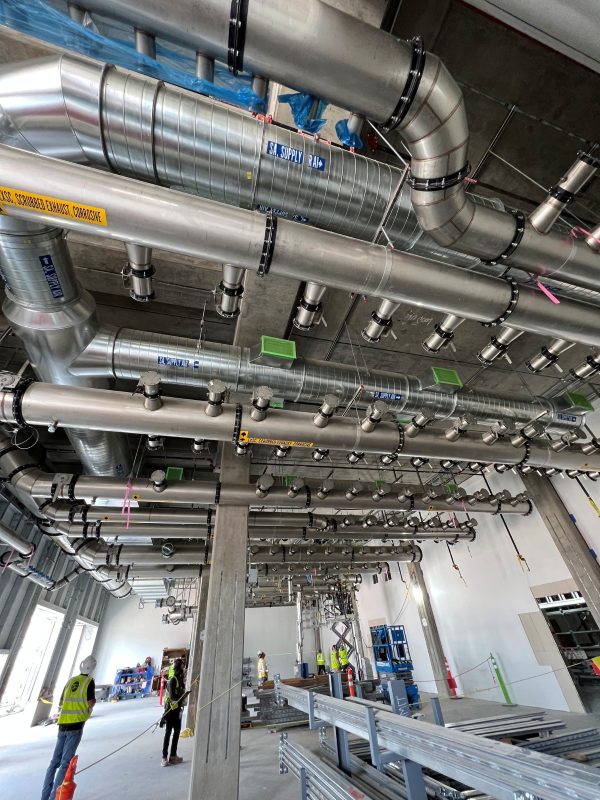 Round process exhaust mains and branch drops hung overhead in a fab building under construction