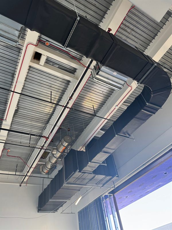 Insulated rectangular HVAC supply duct with a damper and branch runs hung below a steel deck