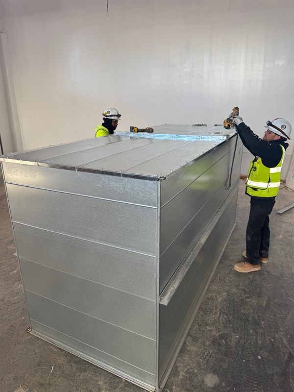 Two Harris & Hart workers assembling a large galvanized rectangular plenum on site