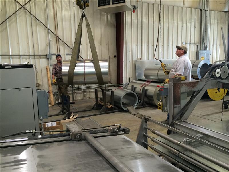 Shop workers moving a coil of sheet steel by overhead hoist