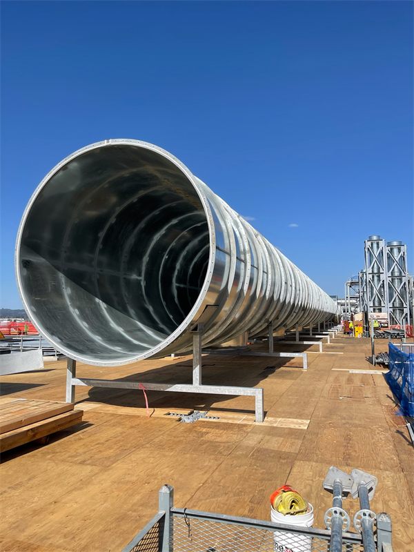 Large-diameter flanged round exhaust duct on supports across a rooftop deck