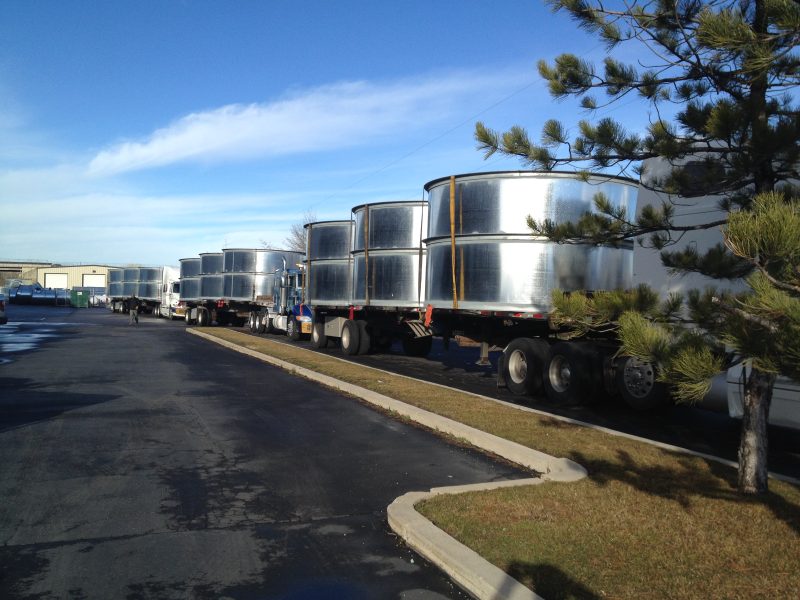 Line of flatbed trucks loaded with large round duct sections parked along a street