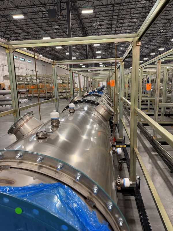 Long run of flanged stainless steel round duct set in steel support racks inside a large building