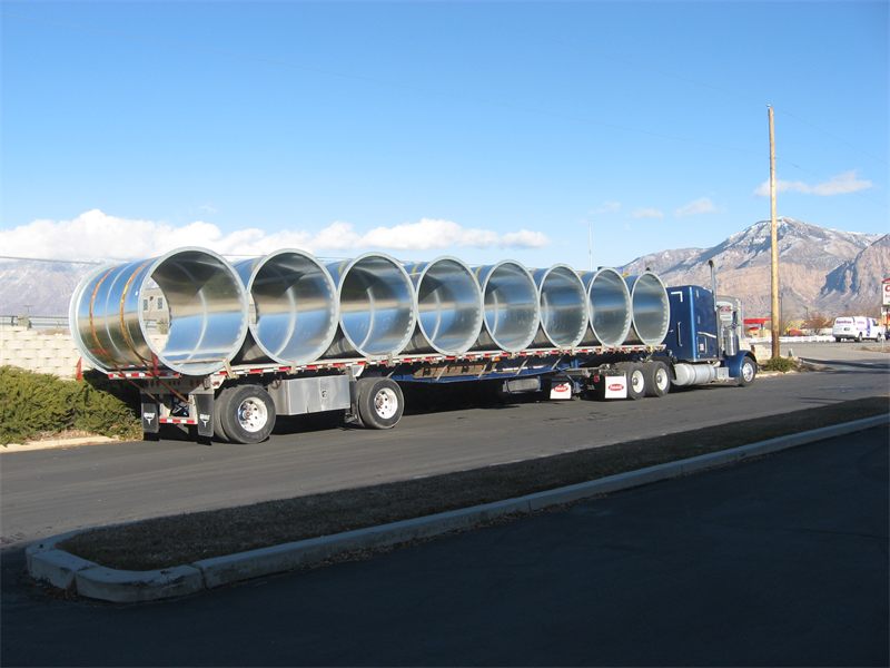Flatbed loaded with large round duct sections, mountains behind