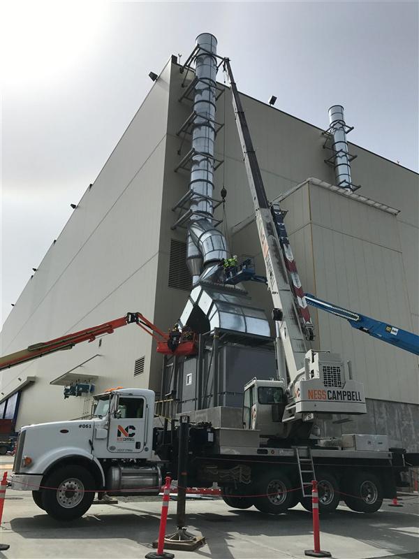Exhaust stack installation by crane on an industrial building